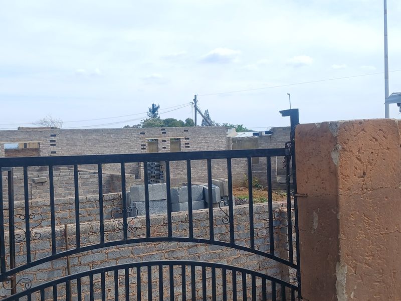 View of an unfinished residential property construction site featuring a metal gate and exposed brick boundary walls.