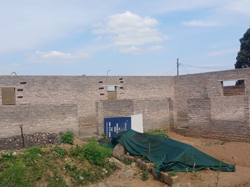 An unfinished residential construction site showing exposed brick masonry walls and open window frames in a rear yard setting.
