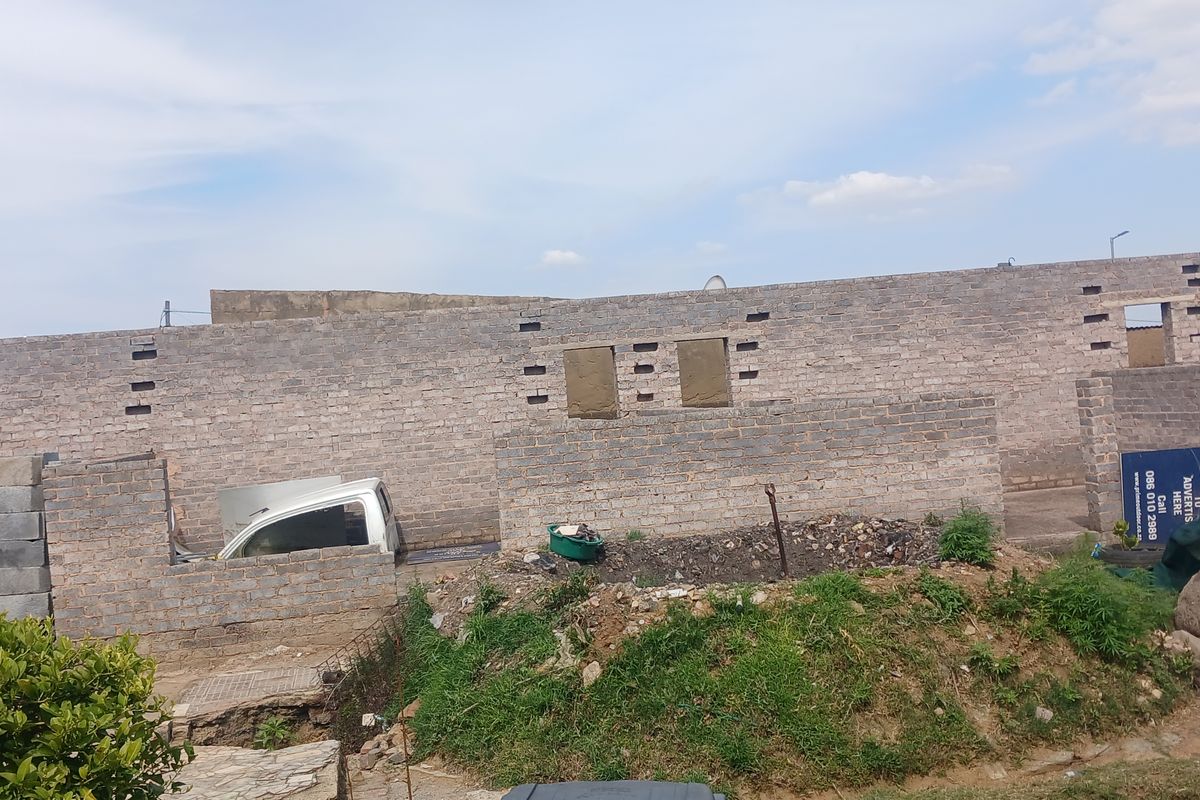 An unfinished brick masonry structure in the rear yard, showing ongoing construction work and unlandscaped grounds.