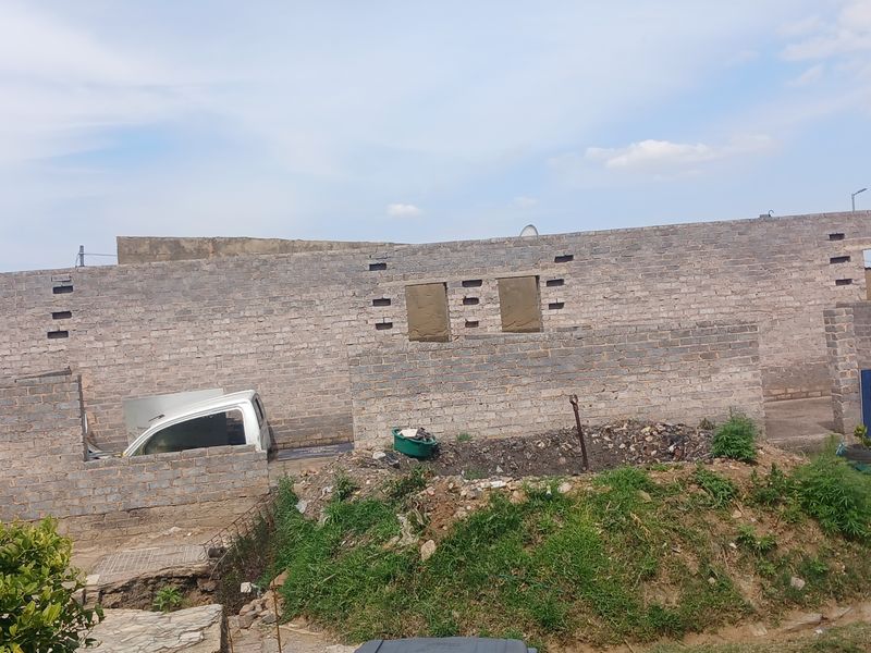 An unfinished brick masonry structure in the rear yard, showing ongoing construction work and unlandscaped grounds.