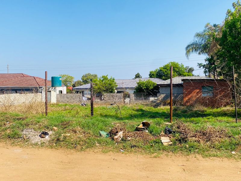 A vacant residential plot featuring perimeter fencing, a small brick outbuilding, and an existing water storage tank, situated in a residential area.