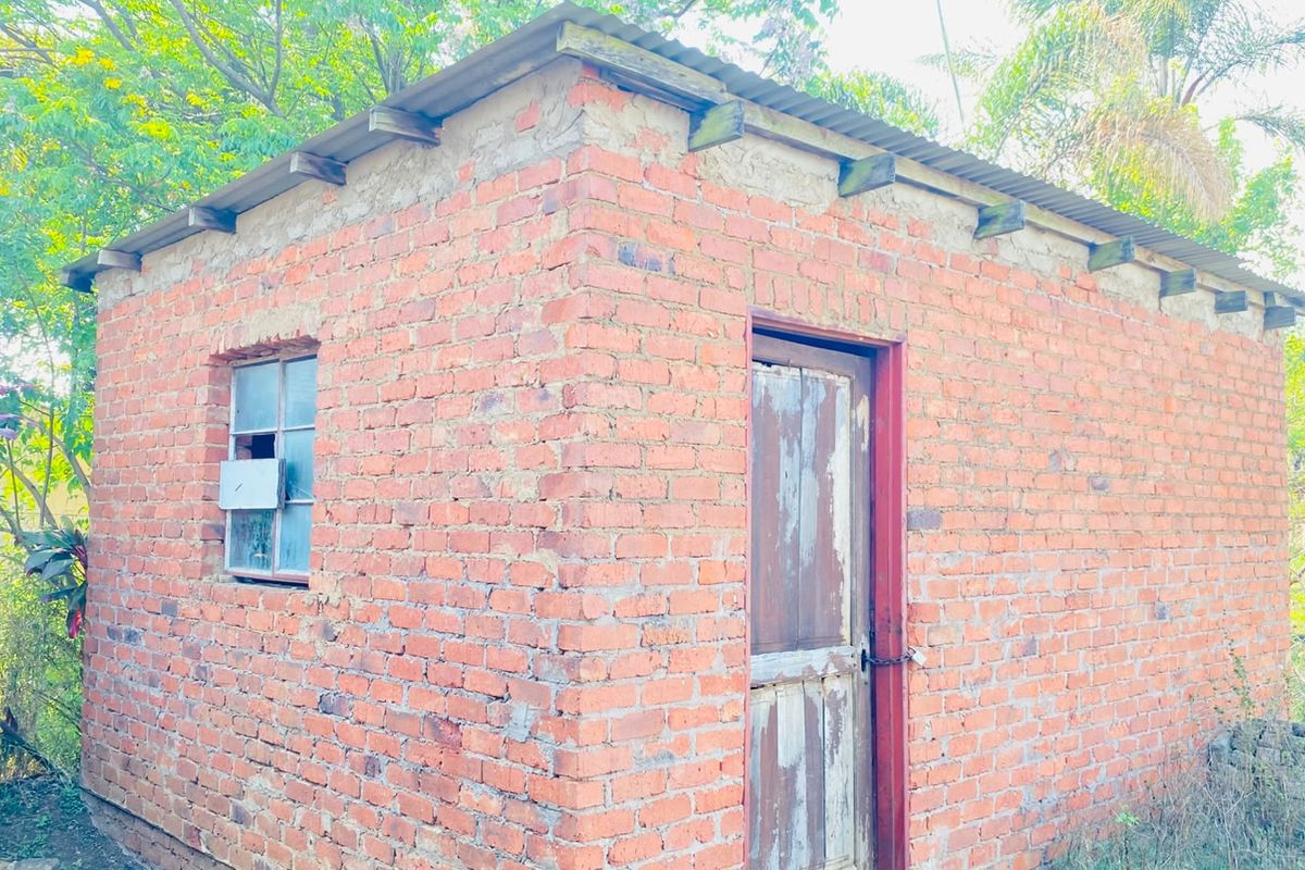 A small, detached brick outbuilding featuring a corrugated metal roof, timber door, and steel-framed window, currently in need of maintenance and repair.