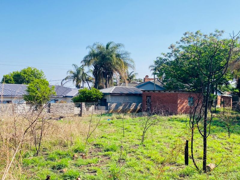 A view of the rear section of the residential land, featuring perimeter fencing, a brick boundary wall, and established trees.