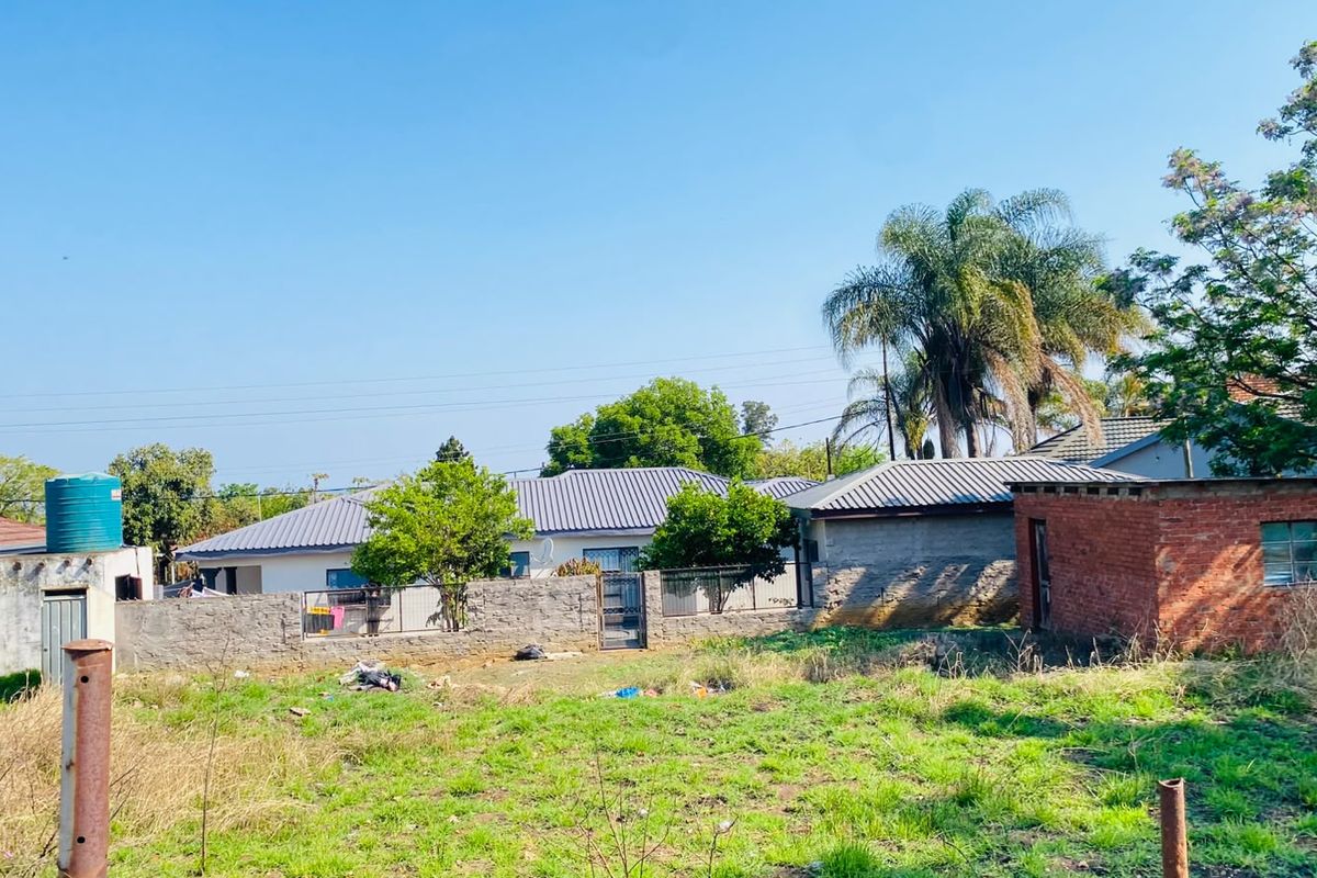 A view of a vacant residential plot featuring a boundary wall, a water storage tank, and a small brick outbuilding structure.