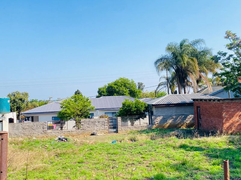 A view of a vacant residential plot featuring a boundary wall, a water storage tank, and a small brick outbuilding structure.