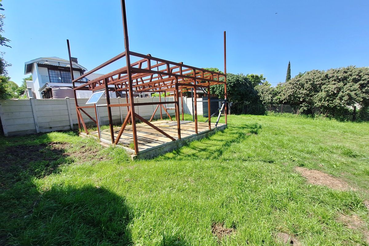 A vacant residential plot featuring a partially constructed steel frame structure on a concrete foundation, enclosed by a precast concrete boundary wall.