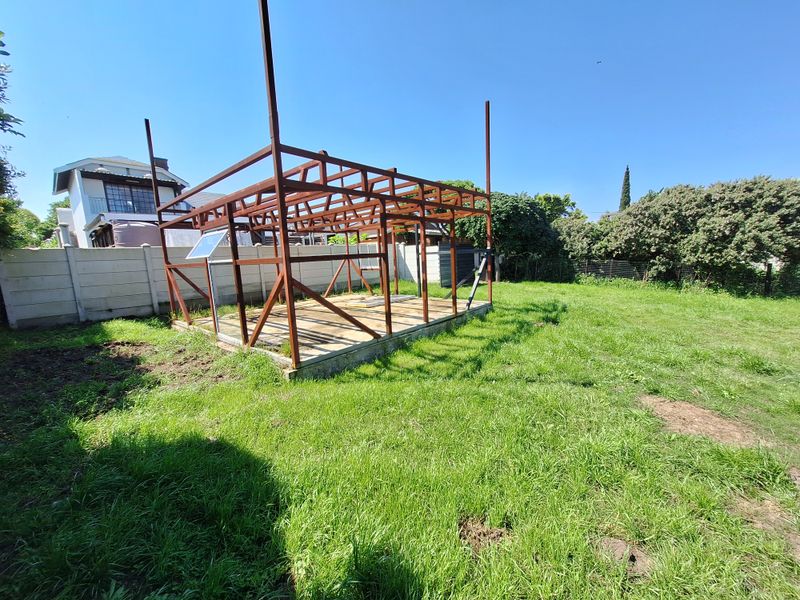 A vacant residential plot featuring a partially constructed steel frame structure on a concrete foundation, enclosed by a precast concrete boundary wall.