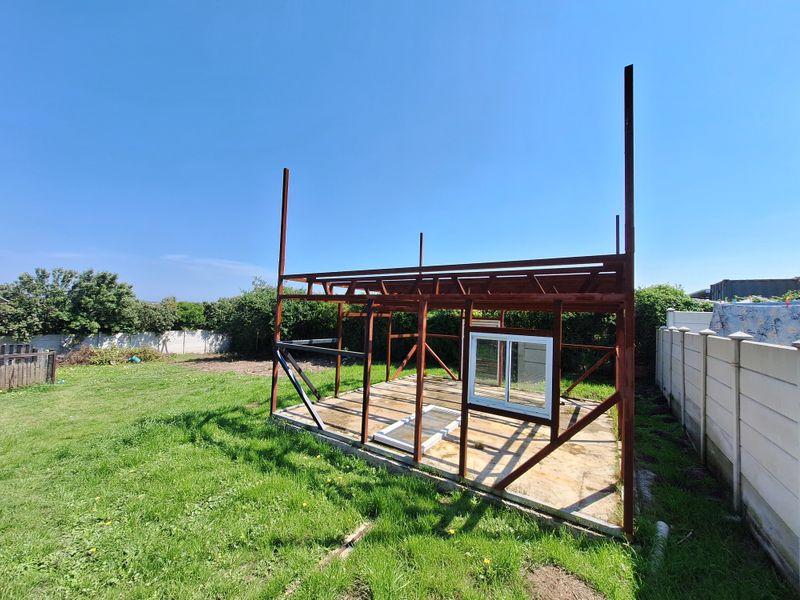 An unfinished steel frame structure on a concrete slab foundation located in a residential backyard, showing the early stages of construction.