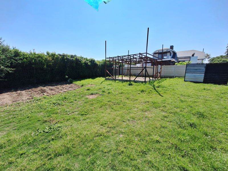 A rear garden area featuring a lawn, established hedging, and an unfinished steel frame structure on a concrete base.