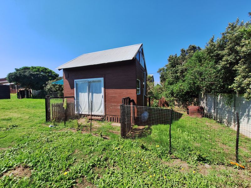 A detached timber-clad structure with a corrugated metal roof, featuring a sliding glass door and enclosed by wire mesh fencing in a garden setting.