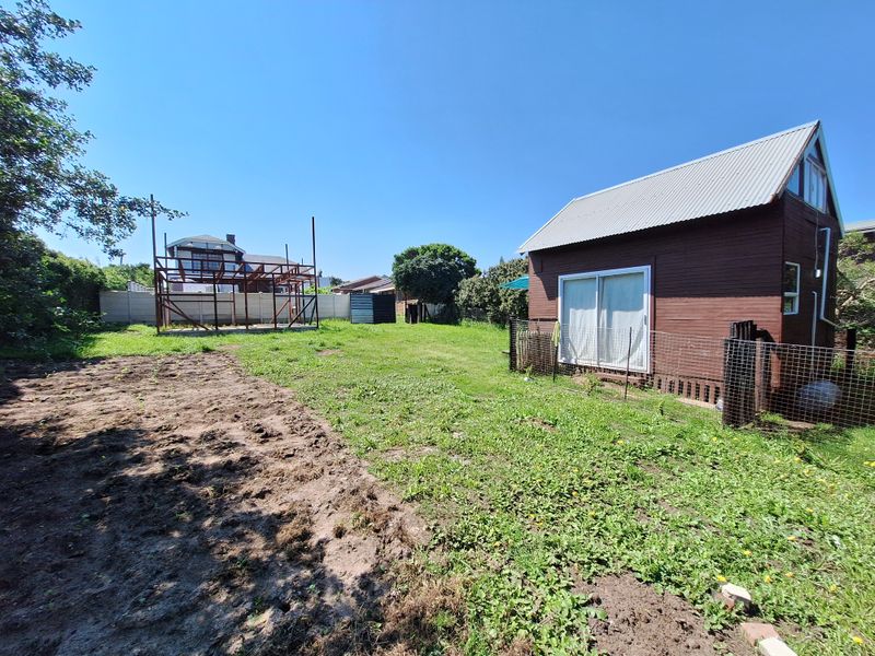 Rear view of the property featuring a small timber-clad structure, a large open garden area, and an unfinished steel frame construction.