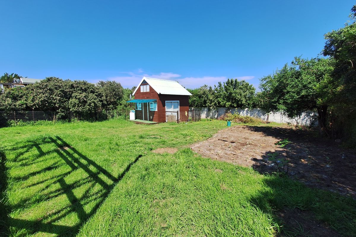 A spacious residential backyard featuring a small timber cabin, established trees, perimeter fencing, and a large grassed area with some cleared ground.