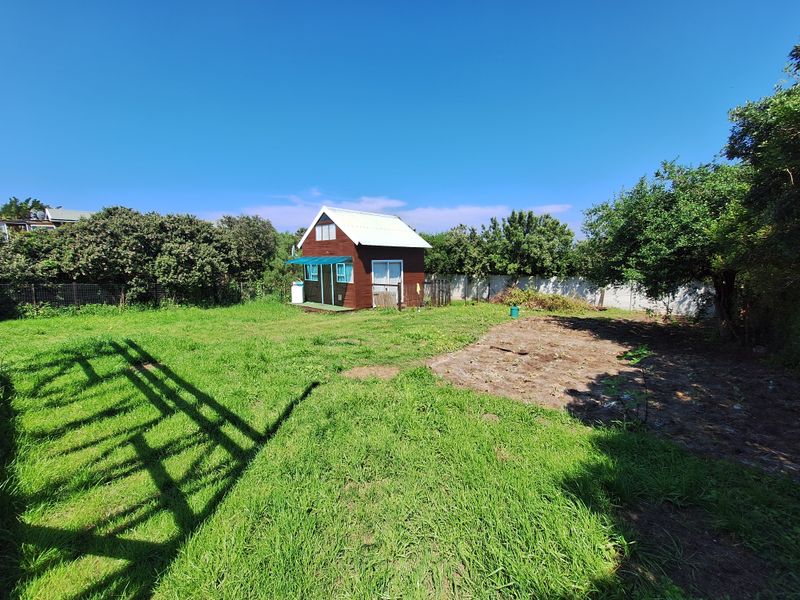 A spacious residential backyard featuring a small timber cabin, established trees, perimeter fencing, and a large grassed area with some cleared ground.