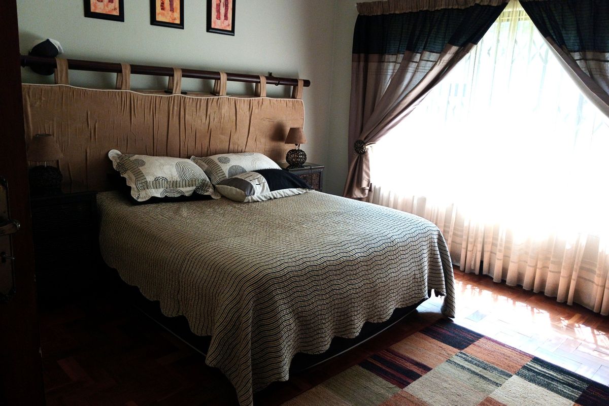 A bedroom featuring warm-toned parquet flooring and large windows dressed with curtains, providing a comfortable and functional sleeping space.