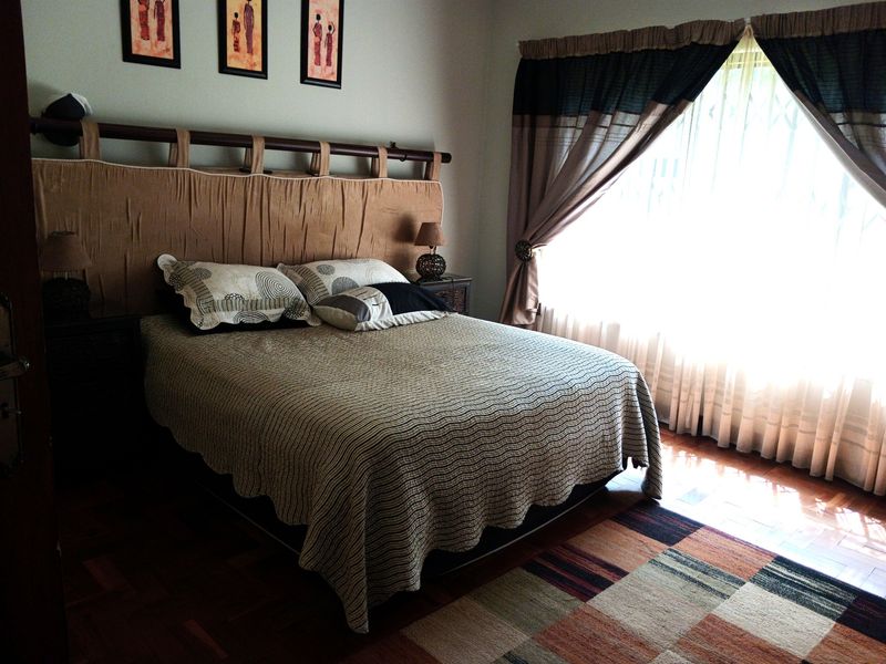 A bedroom featuring warm-toned parquet flooring and large windows dressed with curtains, providing a comfortable and functional sleeping space.
