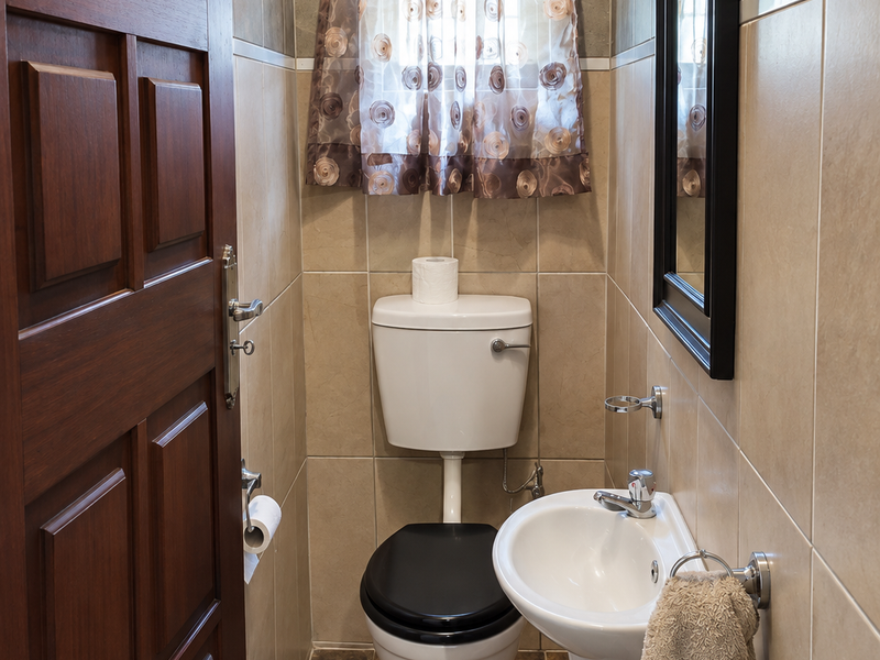A compact guest bathroom featuring a pedestal basin, toilet, and neutral wall tiling with a solid timber door.