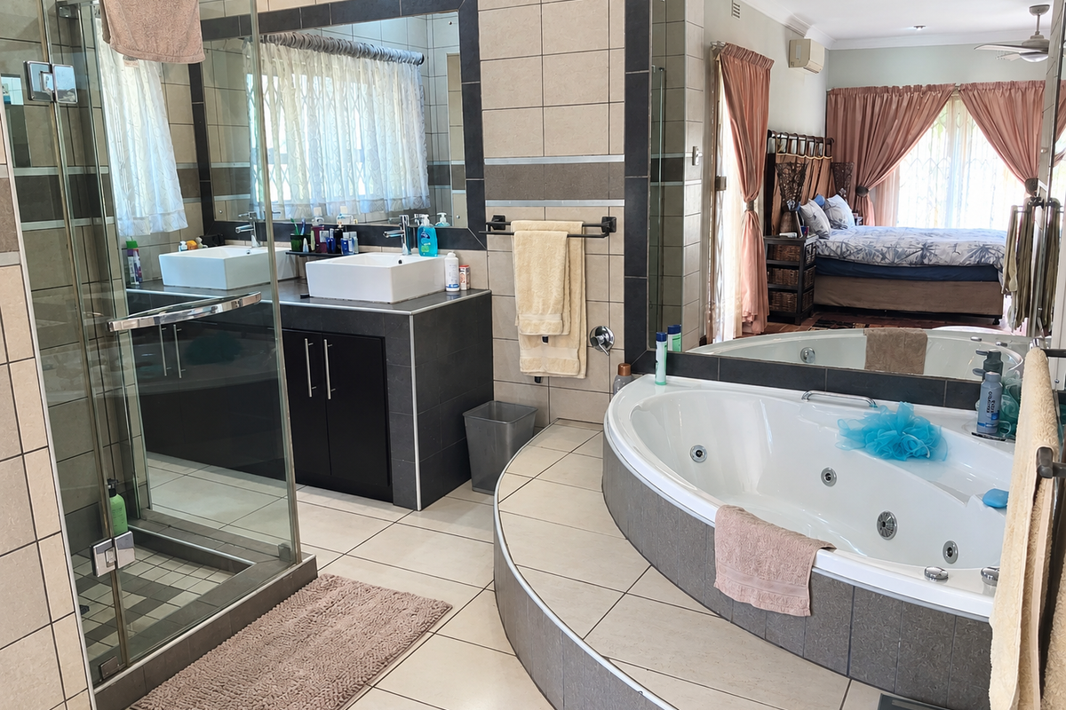 Spacious en-suite bathroom featuring a glass-enclosed shower, a modern vessel sink vanity, and a raised jetted bathtub with tiled finishes.