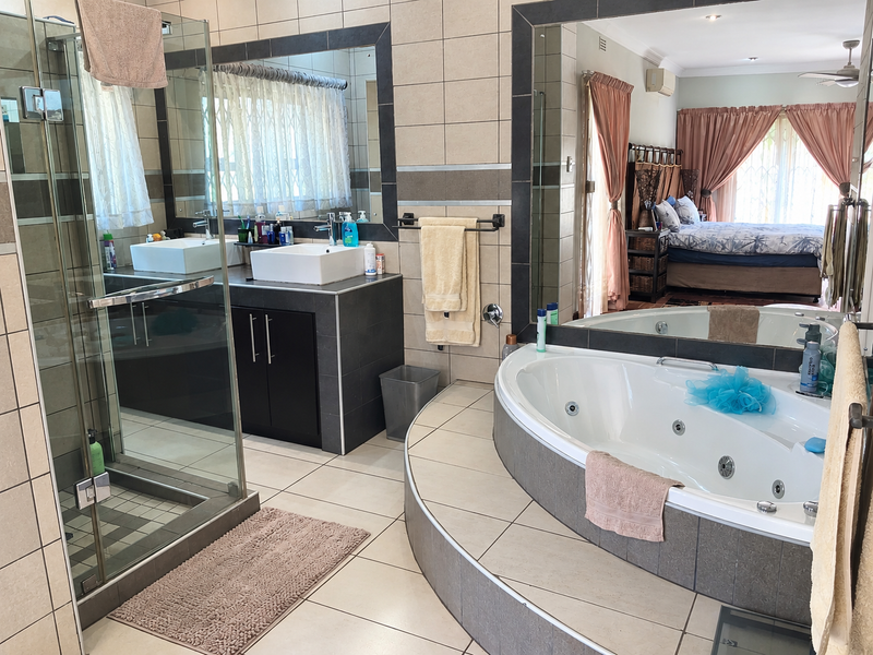 Spacious en-suite bathroom featuring a glass-enclosed shower, a modern vessel sink vanity, and a raised jetted bathtub with tiled finishes.