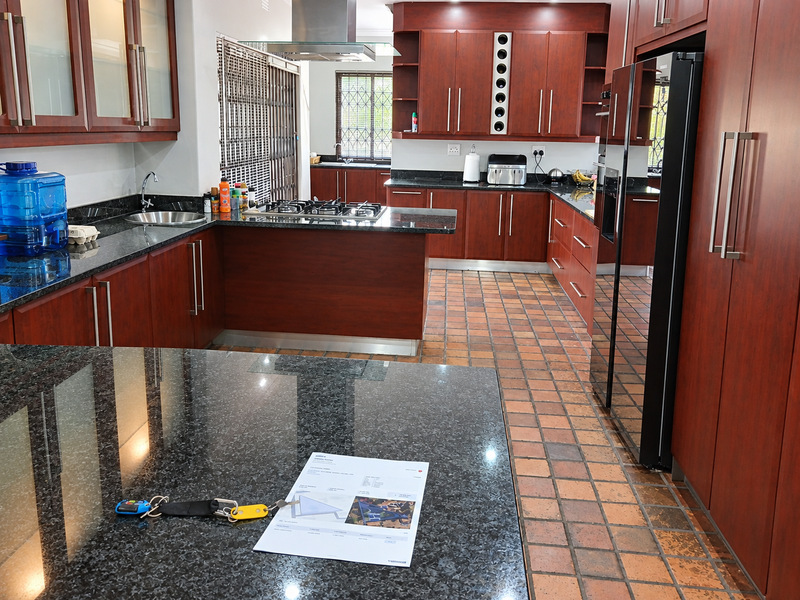 Spacious kitchen featuring cherry wood cabinetry, granite countertops, gas hob with extractor, and durable terracotta flooring, offering ample storage and workspace.