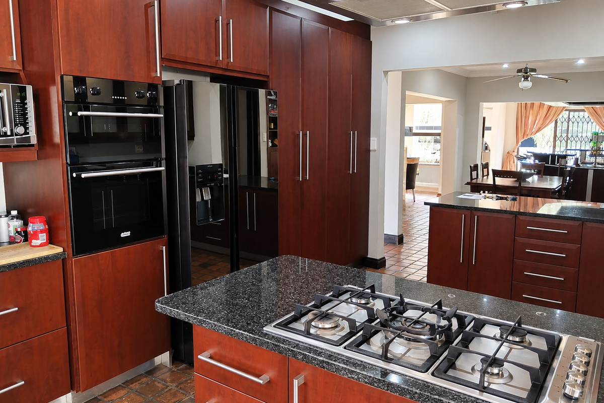 Spacious kitchen featuring dark wood cabinetry, granite countertops, a central island with a gas cooktop, and integrated appliances, flowing into the dining area.