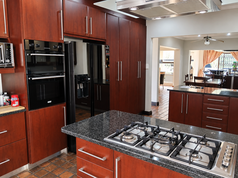 Spacious kitchen featuring dark wood cabinetry, granite countertops, a central island with a gas cooktop, and integrated appliances, flowing into the dining area.
