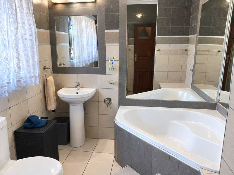 A well-maintained bathroom featuring a corner bathtub, pedestal basin, and neutral-toned wall and floor tiling with a large vanity mirror.