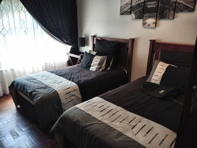A bedroom featuring dark parquet flooring and a window fitted with a security gate.
