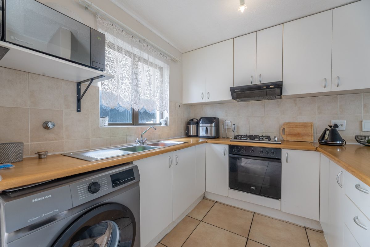 A functional kitchen featuring white cabinetry, laminate countertops, a built-in oven with gas hob, and tiled flooring with integrated laundry plumbing.