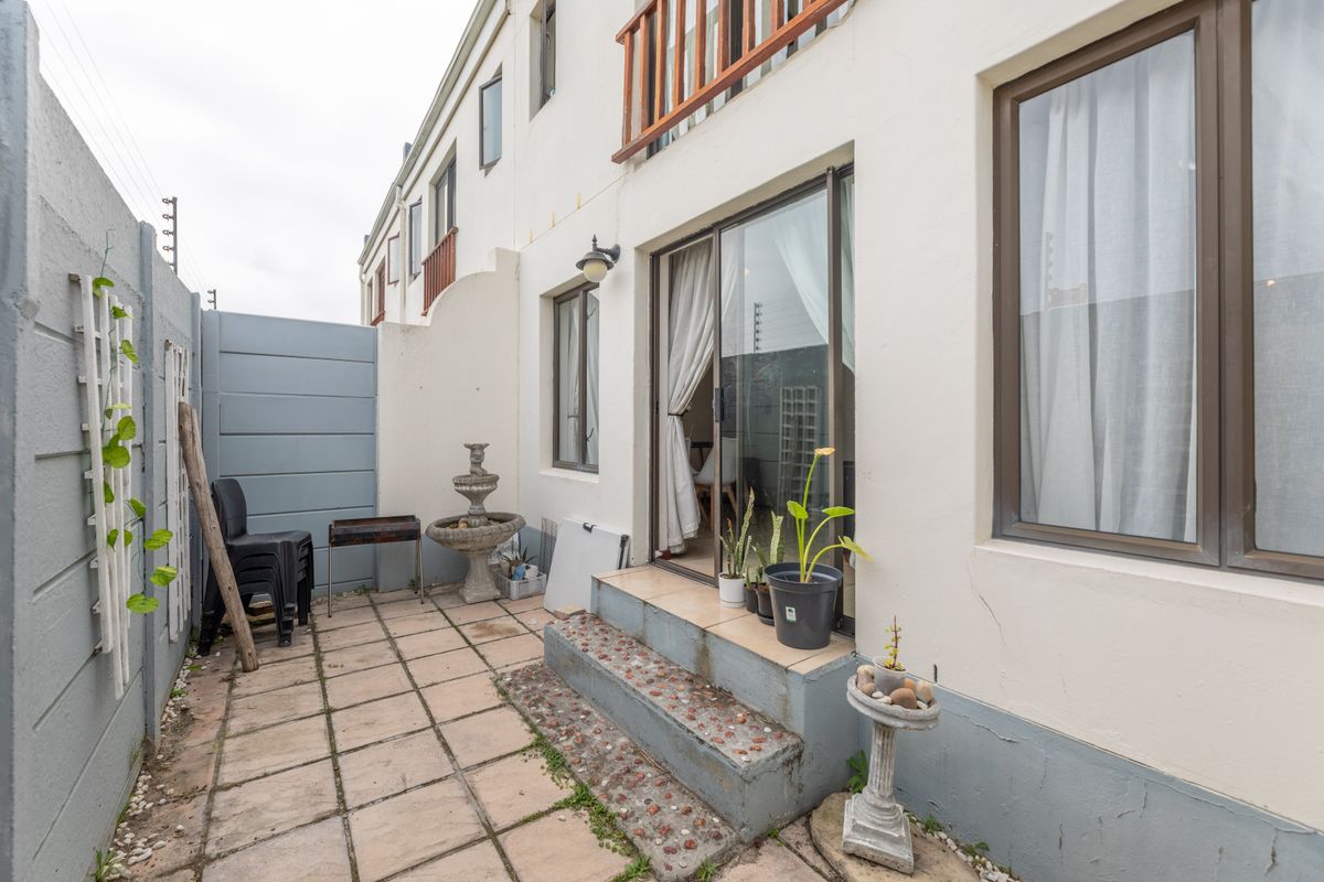 Rear exterior patio area featuring paved flooring, sliding door access, and concrete boundary walls, providing a functional outdoor space for the townhouse.