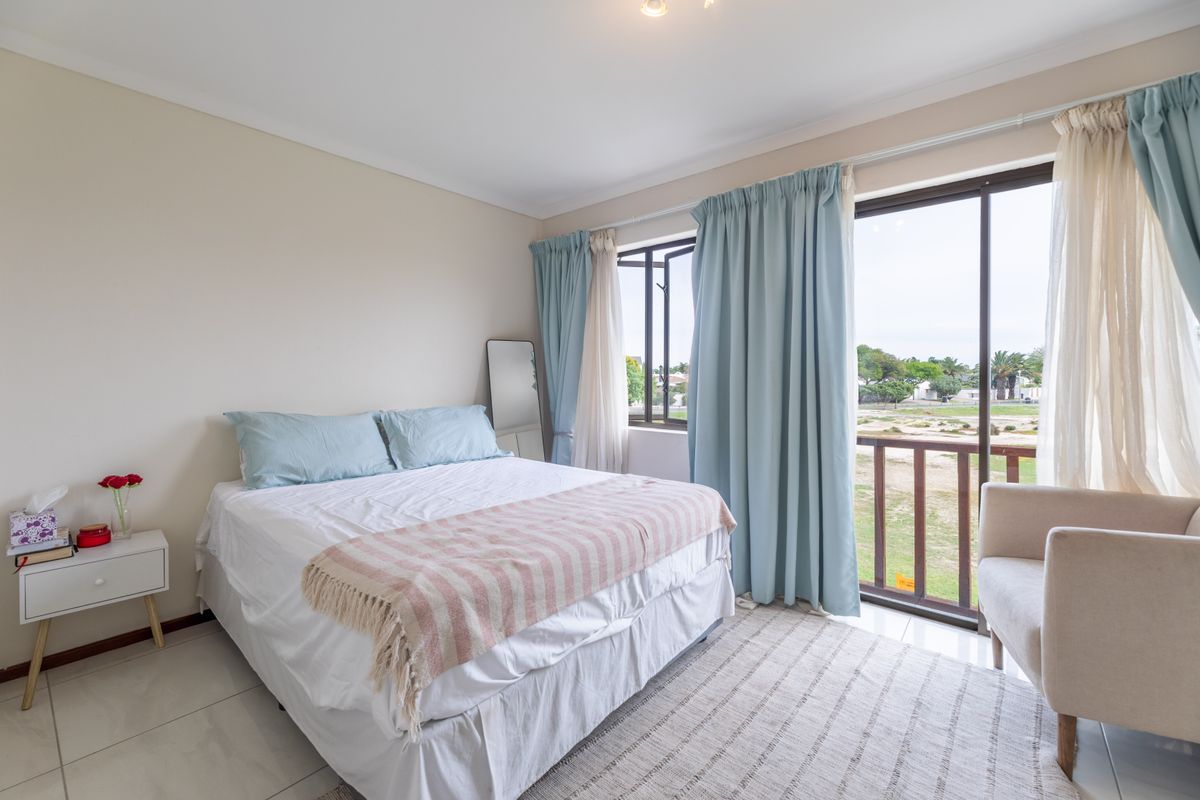 A bright bedroom featuring tiled flooring, a sliding glass door leading to a balcony, and large windows providing natural light and outdoor views.