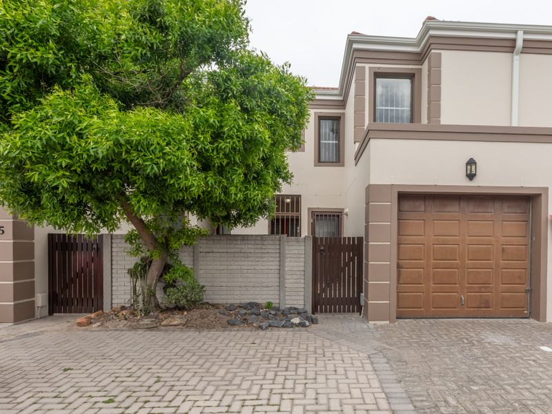 Front elevation of a townhouse featuring a paved driveway, integrated garage, and secure gated entrance with established landscaping.