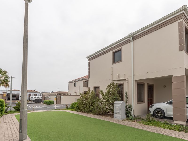 Front view of a townhouse featuring a paved driveway, carport, and a well-maintained artificial lawn area within a secure complex.
