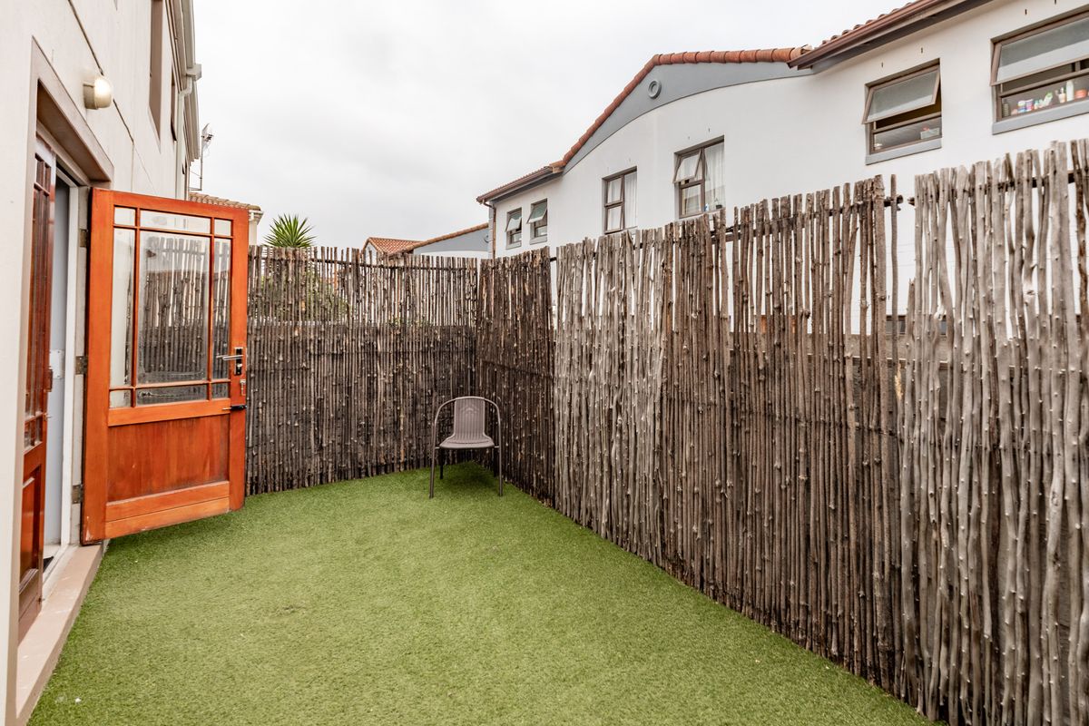 A private rear courtyard area featuring artificial turf and natural bamboo fencing, accessible via a timber door from the main townhouse structure.