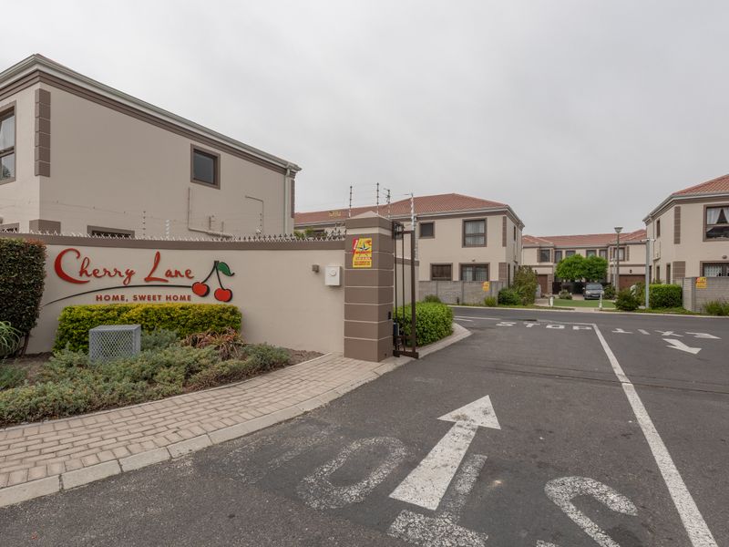 Entrance view of Cherry Lane townhouse complex featuring paved driveway, security gate, and perimeter electric fencing.