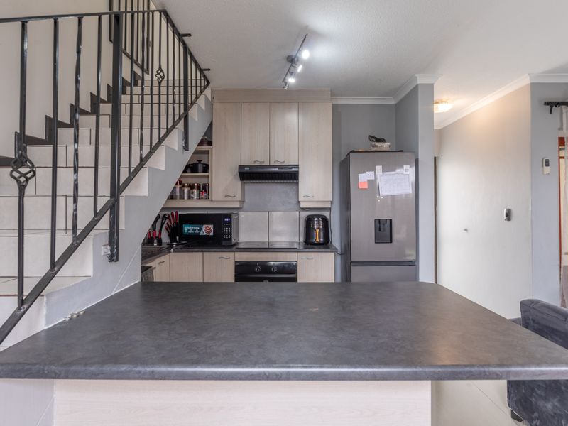 Open plan kitchen featuring built-in cabinetry, integrated appliances, and a breakfast counter, situated adjacent to a staircase with a metal railing.