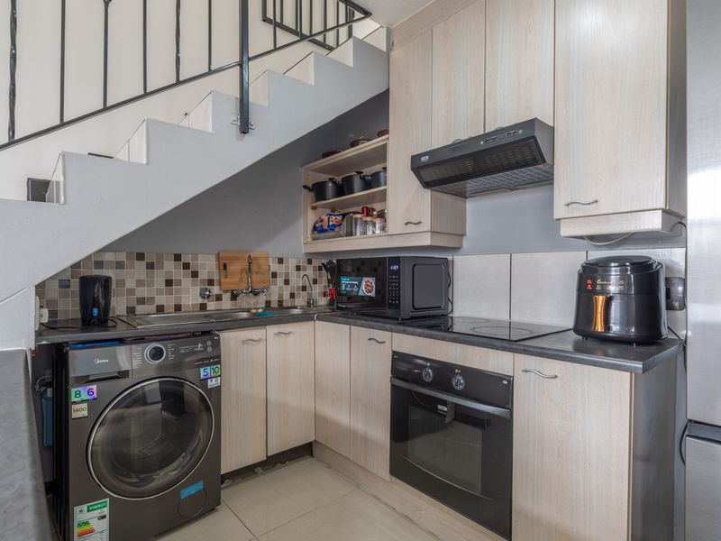 Compact kitchen featuring light wood-finish cabinetry, built-in oven, electric hob, extractor fan, and tiled backsplash, efficiently tucked under the staircase.