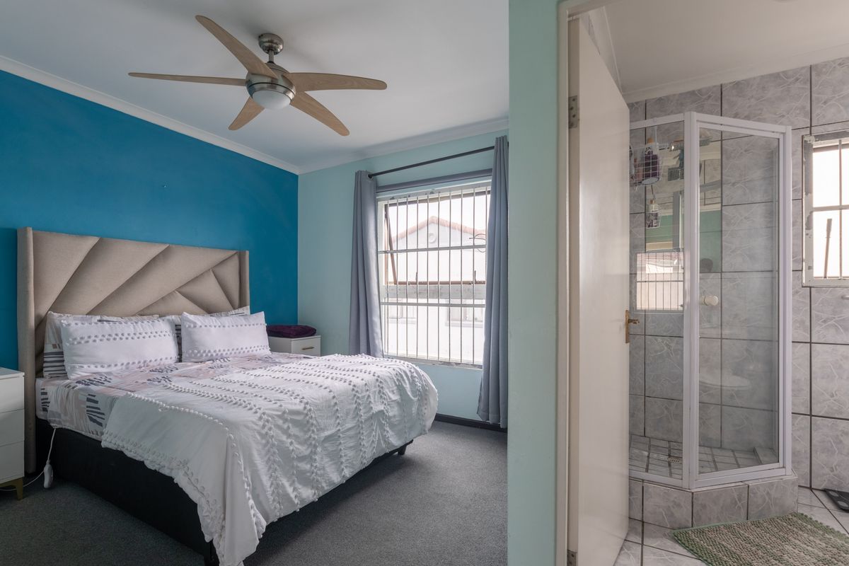 A bedroom featuring a ceiling fan and security bars on the window, with an adjoining en-suite bathroom containing a tiled shower enclosure.