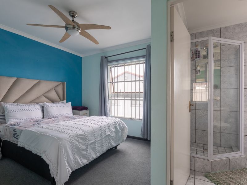 A bedroom featuring a ceiling fan and security bars on the window, with an adjoining en-suite bathroom containing a tiled shower enclosure.