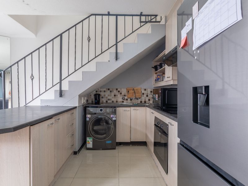 Compact kitchen featuring light wood cabinetry, dark laminate countertops, tiled backsplash, and integrated appliances, efficiently utilizing space beneath the staircase.
