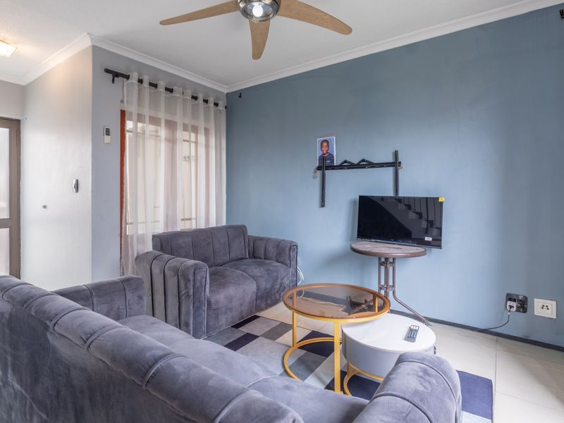 A living room featuring tiled flooring, a ceiling fan, and a sliding glass door providing access to the exterior.