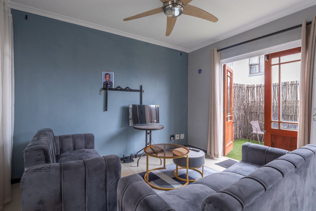 A living room featuring a ceiling fan, tiled flooring, and wooden french doors providing direct access to an outdoor patio area.