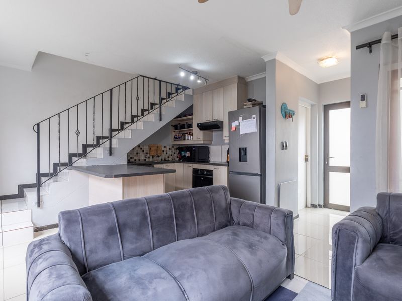Open-plan living area featuring a kitchen with built-in cabinetry, a staircase with metal balustrade, and tiled flooring leading to an exterior door.