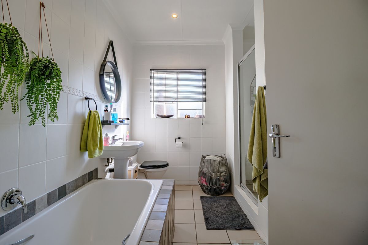 A clean and functional bathroom featuring a pedestal basin, a built-in bathtub, and a separate shower enclosure with neutral wall and floor tiling.