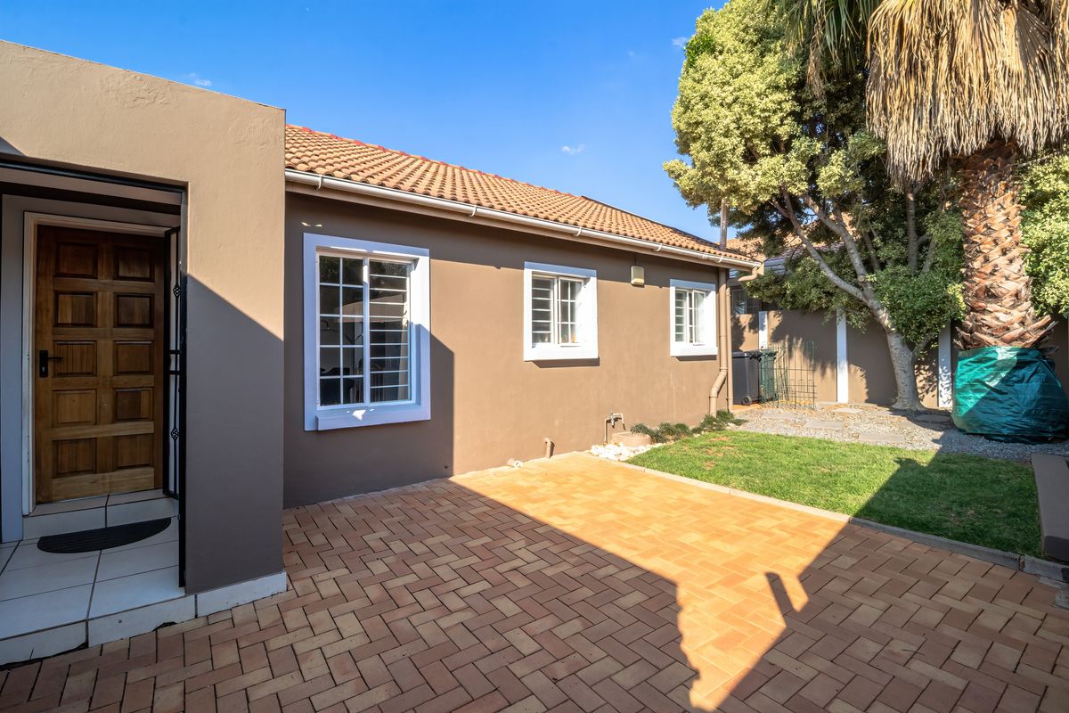 A well-maintained rear exterior view featuring a brick-paved patio, a small lawn area, and a secure wooden entrance door.