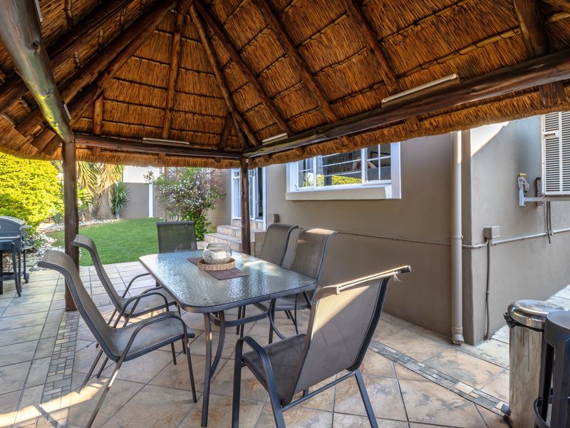 A covered outdoor patio area featuring a traditional thatched roof and tiled flooring, providing a shaded space for outdoor dining and relaxation.