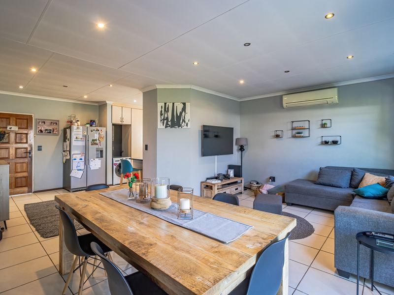 Open-plan living and dining area featuring tiled flooring, recessed lighting, and a wall-mounted air conditioning unit, seamlessly connecting to the kitchen space.