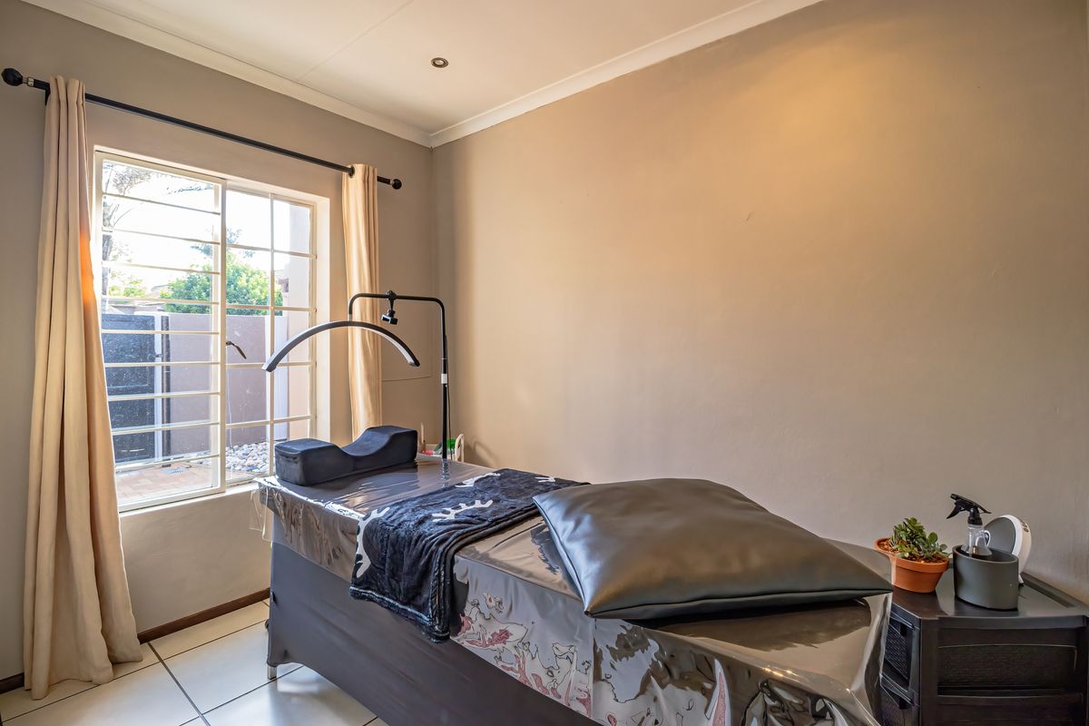 A functional bedroom space featuring tiled flooring, recessed lighting, and a window with security bars, currently utilized as a treatment room.