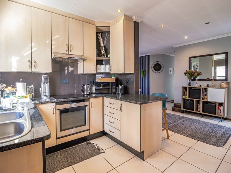 Open-plan kitchen featuring light wood cabinetry, granite countertops, integrated appliances, and tiled flooring, flowing into an adjacent living area.