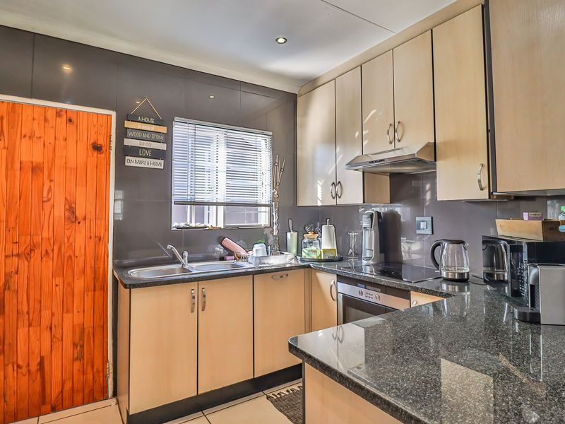 A functional kitchen featuring light wood cabinetry, dark granite countertops, a double basin sink, and integrated appliances including an oven and hob.