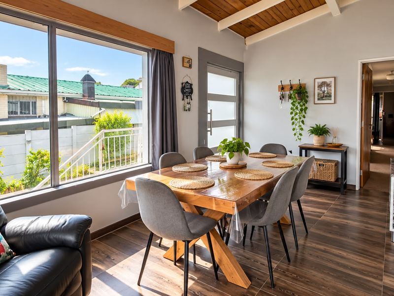 Bright dining area featuring timber-look flooring, exposed timber ceiling beams, and a large window providing natural light and a view of the exterior.